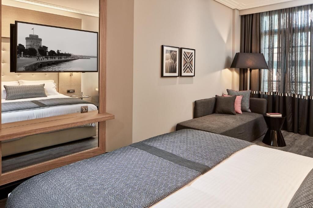Una habitación de hotel con cama, sofá, televisión montada en la pared y lámpara.