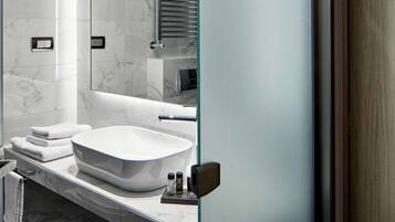 A modern bathroom with a large mirror, white marble tiles, a freestanding bathtub, and a sleek vanity.