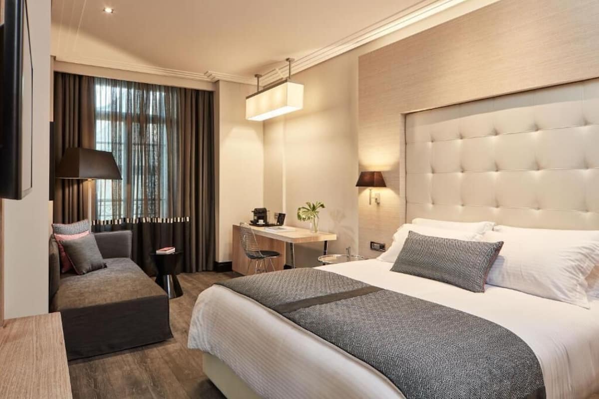 Quarto de hotel moderno com uma cama grande, uma escrivaninha e um espaço para sentar.