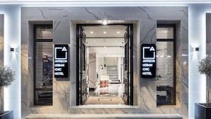 La entrada al Hotel Antigon Urban Chic, con un diseño moderno, que presenta una fachada de mármol y una escalera acogedora.