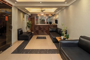 A hotel lobby with a reception desk, seating area, and a ceiling fan.