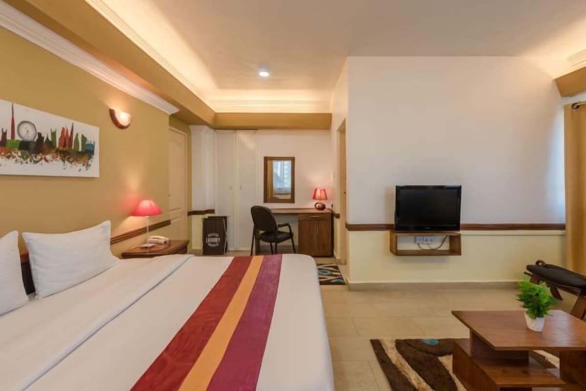 A hotel room with a bed, desk, chair, television, and a small table with a plant.