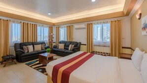 Et rummeligt hotelværelse med en stor seng, to sofaer, et sofabord og udsigt til bybilledet.