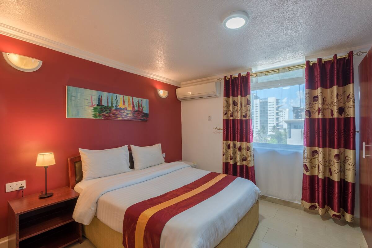 Ein Hotelzimmer mit einem Bett, einem Nachttisch, einem Gemälde und einem Fenster mit Vorhängen.