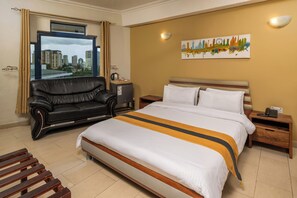 Ein Hotelzimmer mit Bett, einer Ledersofa, einem Nachttisch, einer Wandlampe und Blick auf die Stadt.
