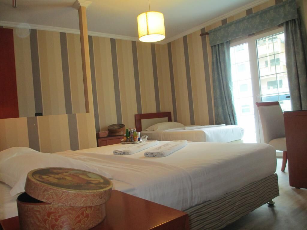 Ett hotellrum med två sängar, ett träbord vid sängen, en lampa och utsikt över staden genom fönstret.