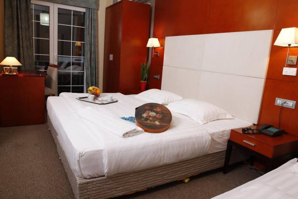 A hotel room with a large bed, a bedside table with a lamp, a small table with a vase of flowers, and a wardrobe.