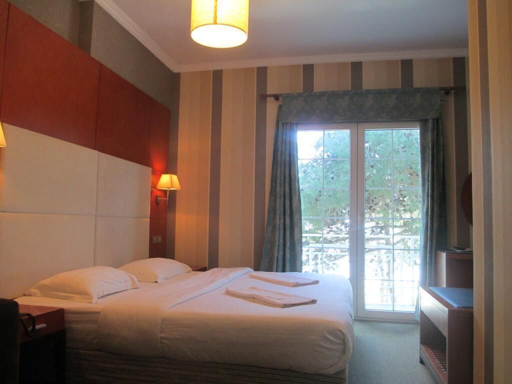 Ett hotellrum med en säng, två sänglampor, en tv och ett fönster med gardiner.