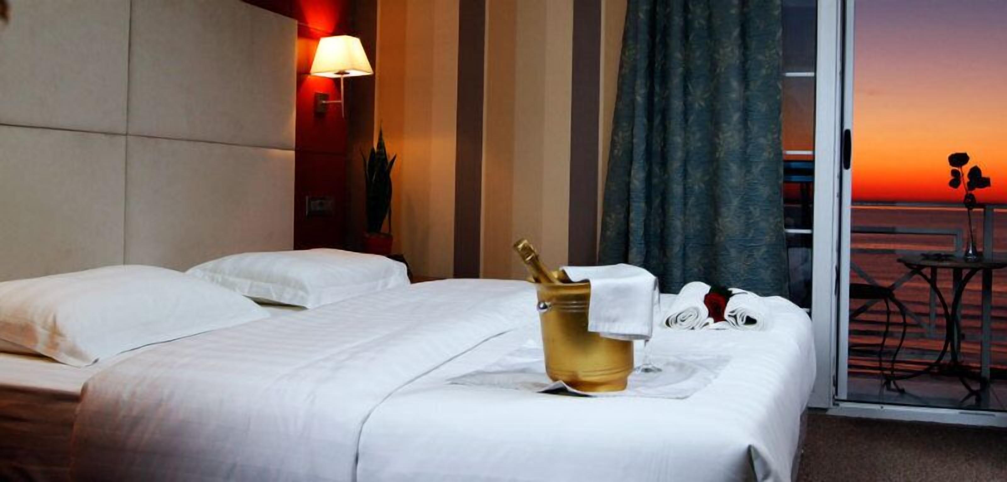 Ett hotellrum med två sängar, en minibar, utsikt över solnedgången och ett bord med en stol vid fönstret.