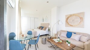 A modern hotel room with a glass dining table, blue chairs, a wooden coffee table, a beige sofa, and a large abstract painting. - Apartamentos Soho Boutique Museo (Málaga)