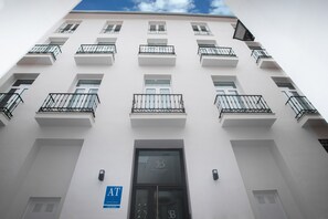 A multi-story building with a white facade, multiple balconies with black railings, and a sign indicating a business or boutique on the ground floor. - Apartamentos Soho Boutique Museo (Málaga)