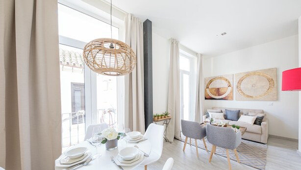 A modern dining area with a white table set for four, a wicker pendant light, and a view of the outdoors through large windows. - Apartamentos Soho Boutique Museo (Málaga)
