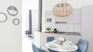 A modern kitchen with white cabinets, a microwave, and a dining area with blue chairs and a white table set for four. - Apartamentos Soho Boutique Museo (Málaga)