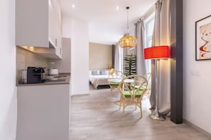 A modern kitchen with a coffee machine, a dining area with a table and chairs, and a living area with a sofa and a lamp. - Apartamentos Soho Boutique Museo (Málaga)