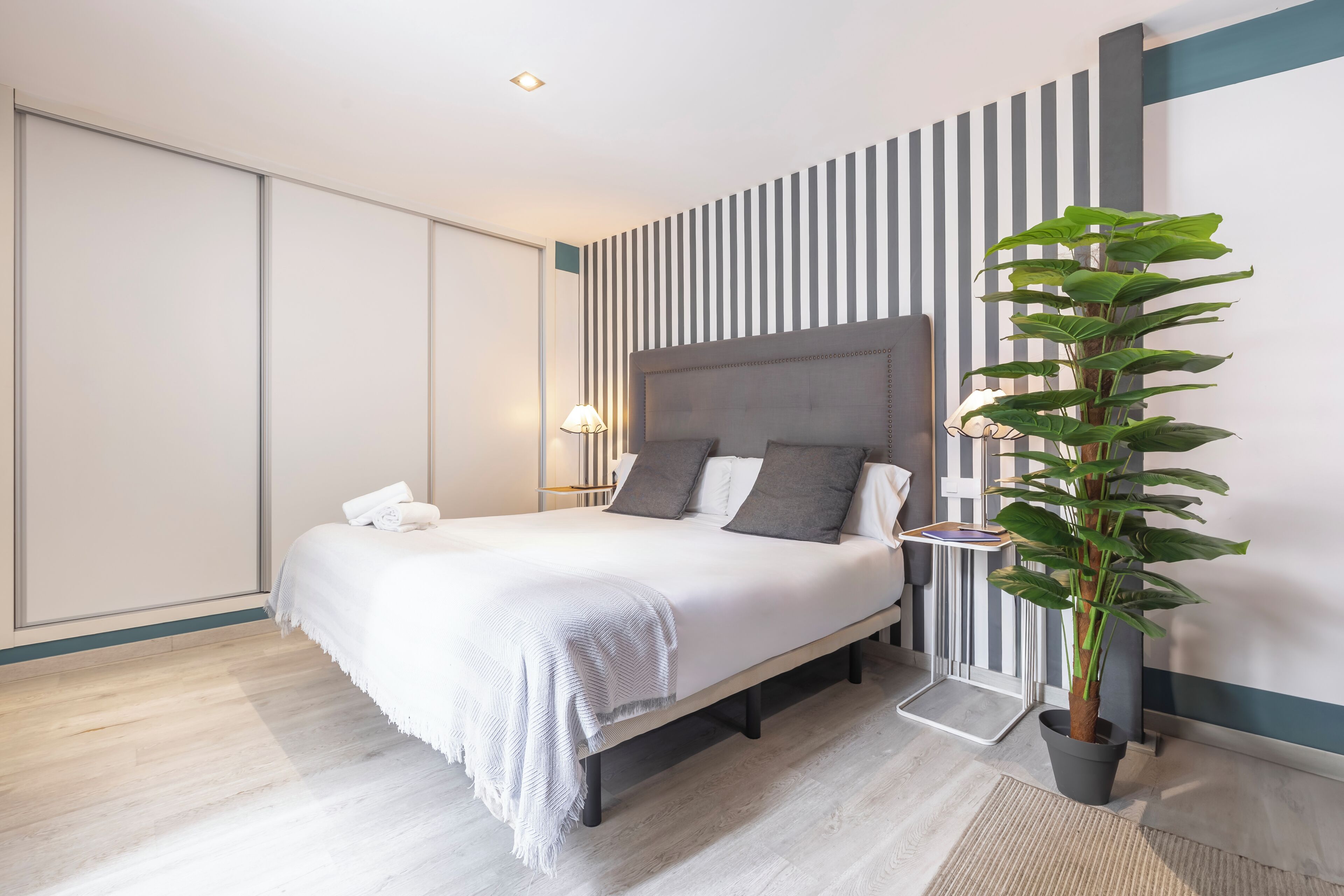A modern bedroom with a bed, bedside table, lamp, and a potted plant.