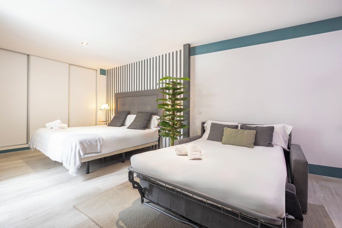 A hotel room with two beds, a large potted plant, and a modern design.