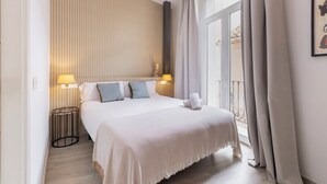A hotel room with a bed, two bedside lamps, a window with curtains, and a view of the outside. - Apartamentos Soho Boutique Museo (Málaga)