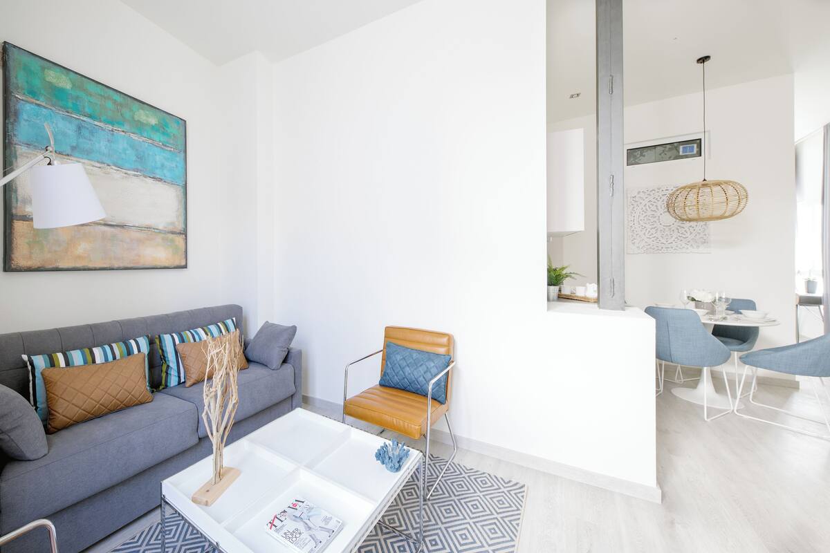 A modern living room with a grey sofa, a coffee table, and a dining area with two chairs.