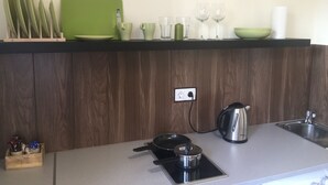Moderni keittiö, jossa on musta työtaso, ruostumattomasta teräksestä valmistettu vedenkeitin, kattila induktioliedellä ja puinen keittiövälineiden säilytysastia.