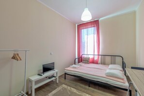 A bedroom with a bed, a TV on a stand, a desk, and a hanging clothes rack.