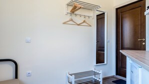 Een kamer met een bed, een klein wit bankje, een kledingrek, een deur en een witte kast.
