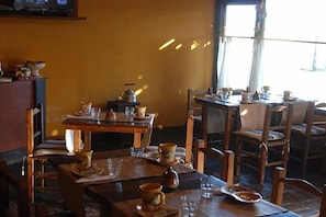Un restaurante con mesas y sillas de madera, una tetera sobre una mesa y varias tazas y platillos.