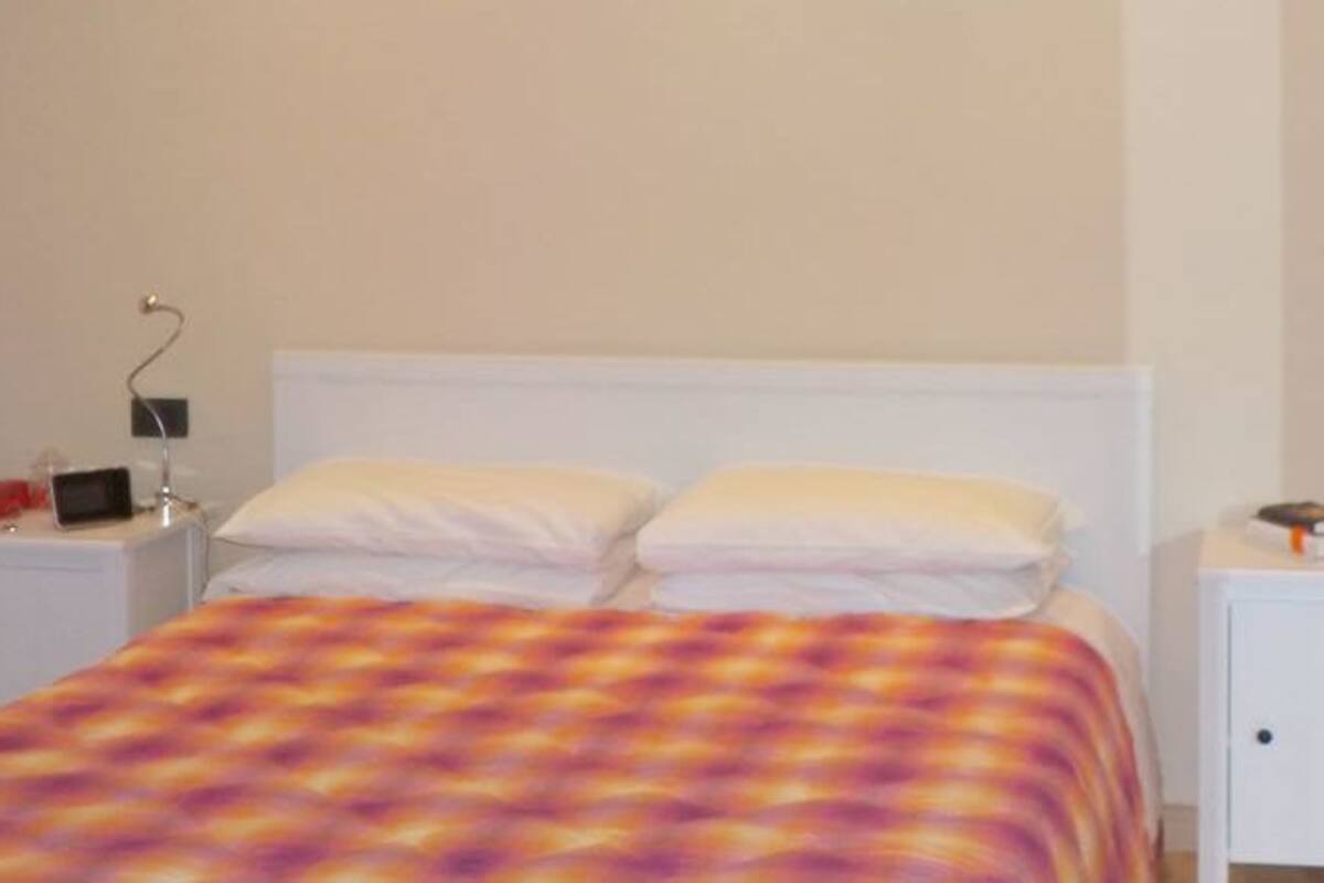 A bedroom with a bed, bedside tables, and a bathroom visible in the background.