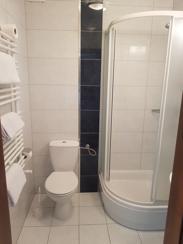 A modern bathroom with a toilet, a shower with a glass door, and a towel rack with multiple towels.