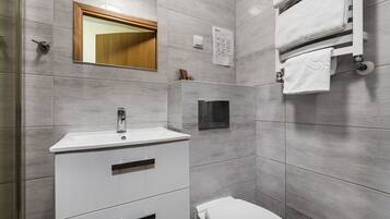 Un baño moderno con un lavamanos blanco, un espejo, un inodoro y un perchero para toallas.
