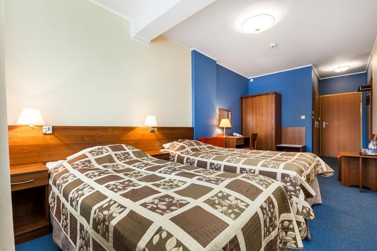 Une chambre d’hôtel avec deux lits, des têtes de lit en bois, une table de chevet, un bureau et une armoire.