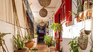 Un passadís estret amb paviment de rajoles, plantes penjants i combinació de parets vermelles i blanques.