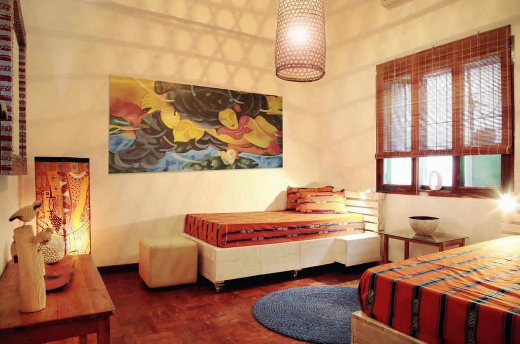A room with a bed, a table with decorative items, a painting on the wall, and a window with blinds.