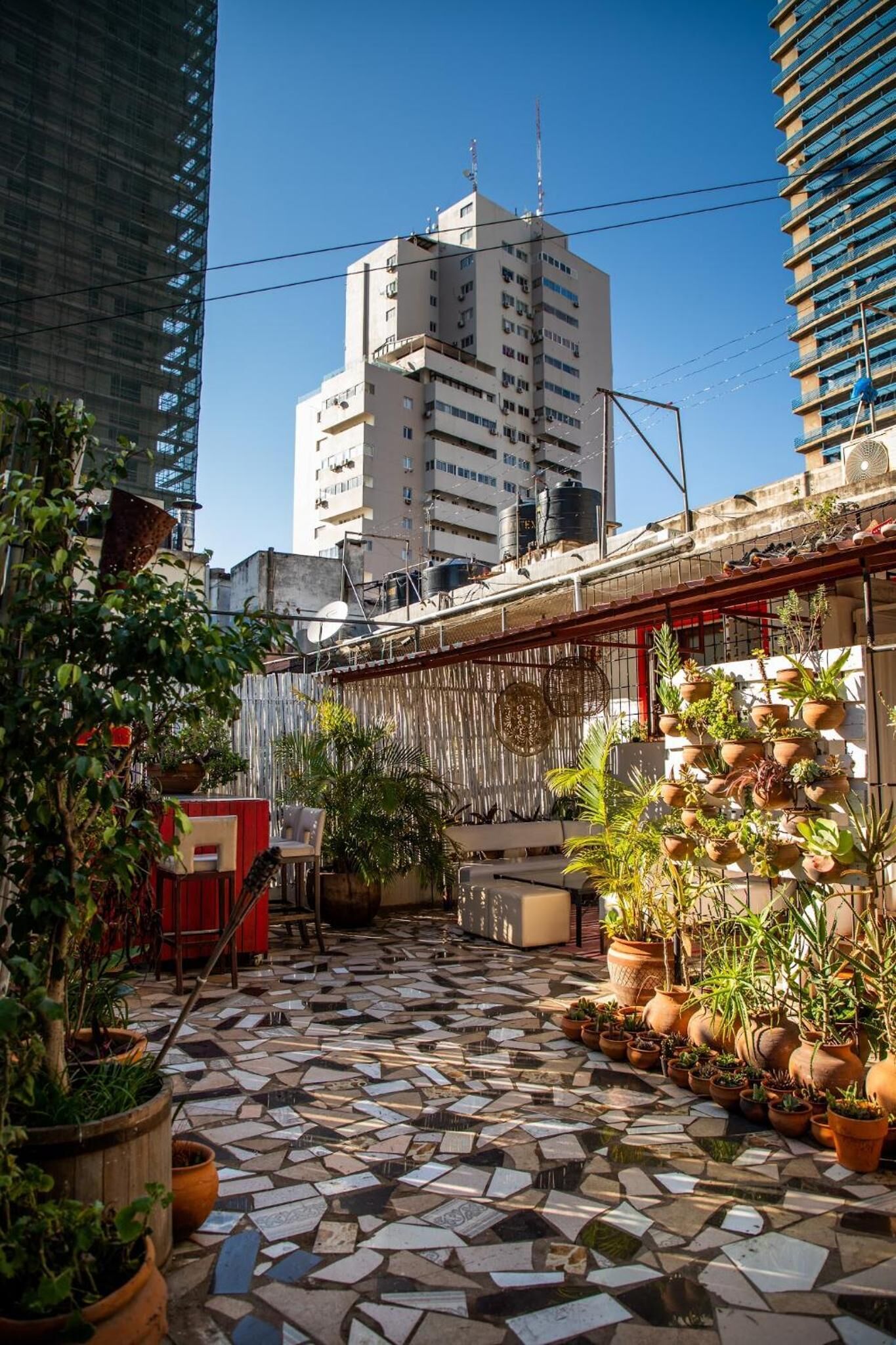 A rooftop patio with a mosaic floor, potted plants, and a red chair.