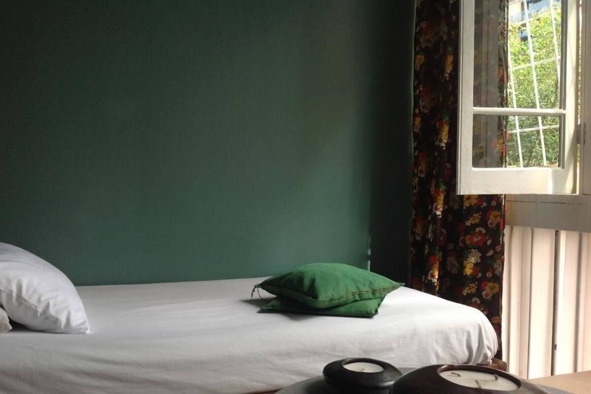 A room with a bed, green walls, a window with curtains, and a table with candles.