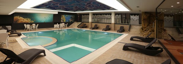 Una piscina interior con sillones de descanso y un mural en la pared.