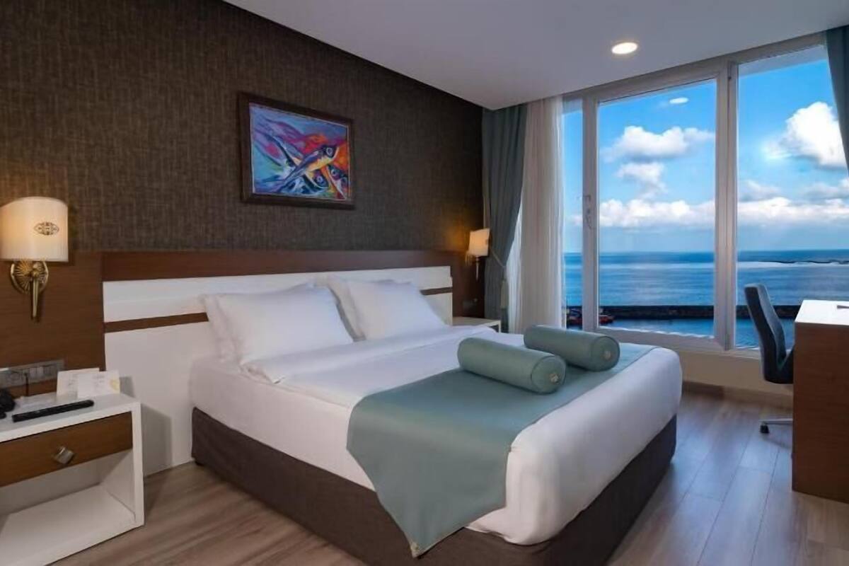 A hotel room with a large bed, two bedside tables, a desk, and a view of the ocean.