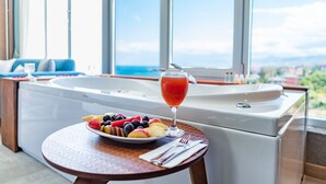 A room with a large window, a bathtub, a fruit bowl, and a glass of red drink. - Tilya Resort Hotel (Akçaabat)