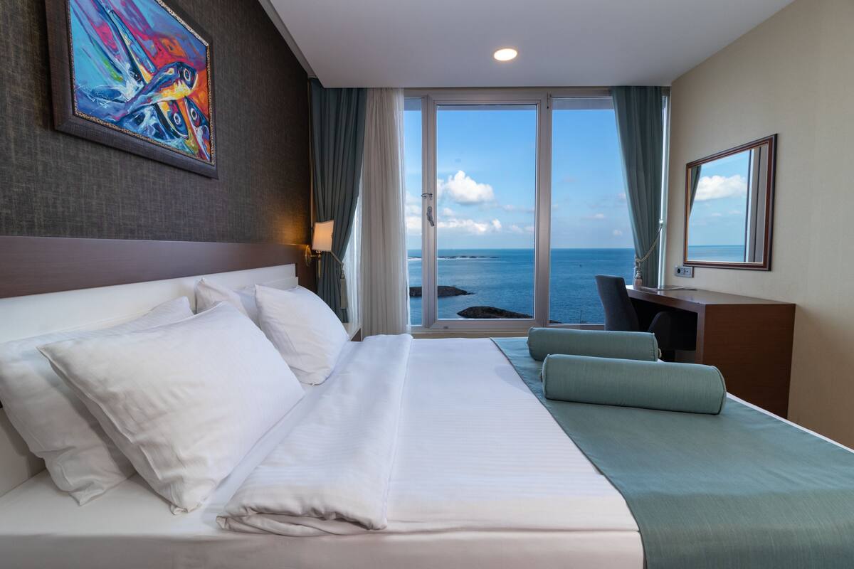 A hotel room with a large bed, a desk, and a view of the ocean.