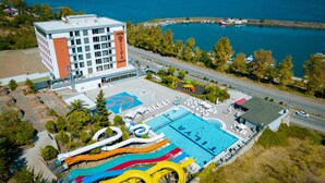 A hotel with a large pool and water slides, surrounded by a scenic view of the sea and a parking area. - Tilya Resort Hotel (Akçaabat)