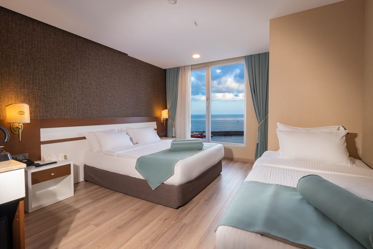 A hotel room with a large bed, a smaller bed, a desk, and a view of the sea.
