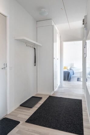 A hallway with a white door, a coat rack, and a black doormat. - Hiisi Homes Lohja (Lohja)