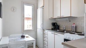 A compact kitchen with white cabinets, a built-in oven, a coffee maker, and a window with a view of buildings. - Hiisi Homes Lohja (Lohja)