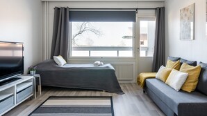 A modern bedroom with a bed, a sofa, a TV, and a window with curtains. - Hiisi Homes Lohja (Lohja)