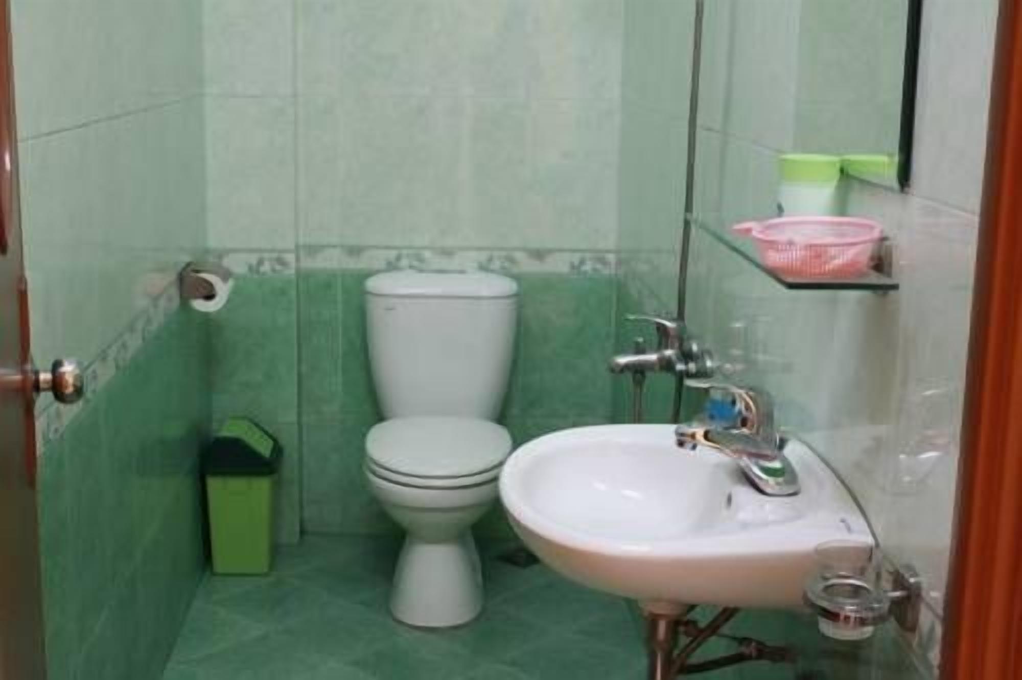 A small bathroom with a toilet, sink, and a green tiled wall.