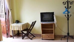 A room with a television on a stand, a chair, and a coat rack. - Phong Lan Guesthouse (Hue)