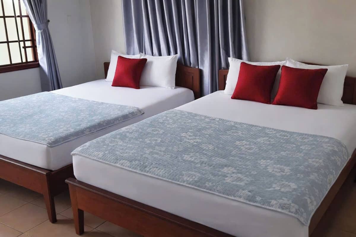 Two double beds with white and red bedding, wooden headboards, and a window with curtains.