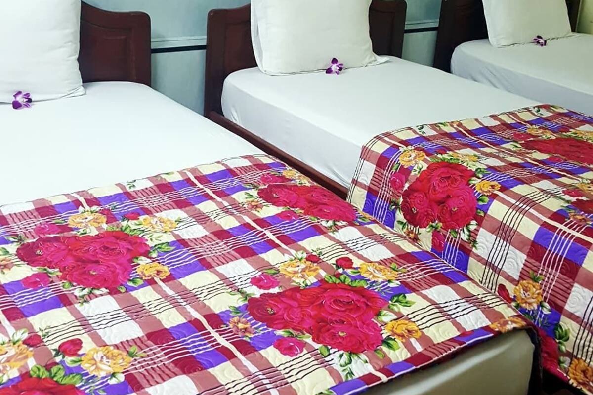 A hotel room with three single beds, each with a floral-patterned bedspread and white pillows.