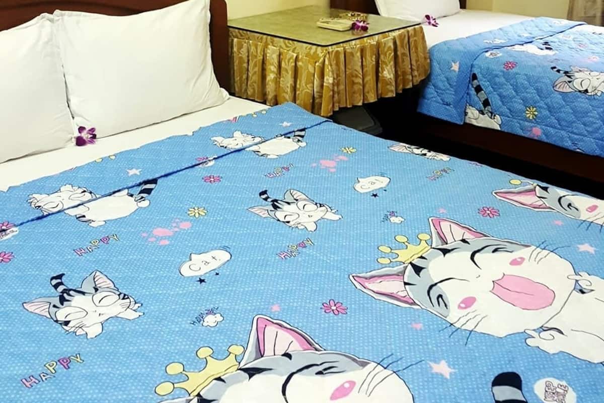 A room with two beds, each covered with blue bedding featuring cartoon cat designs. There is a small table with a gold tablecloth between the beds.