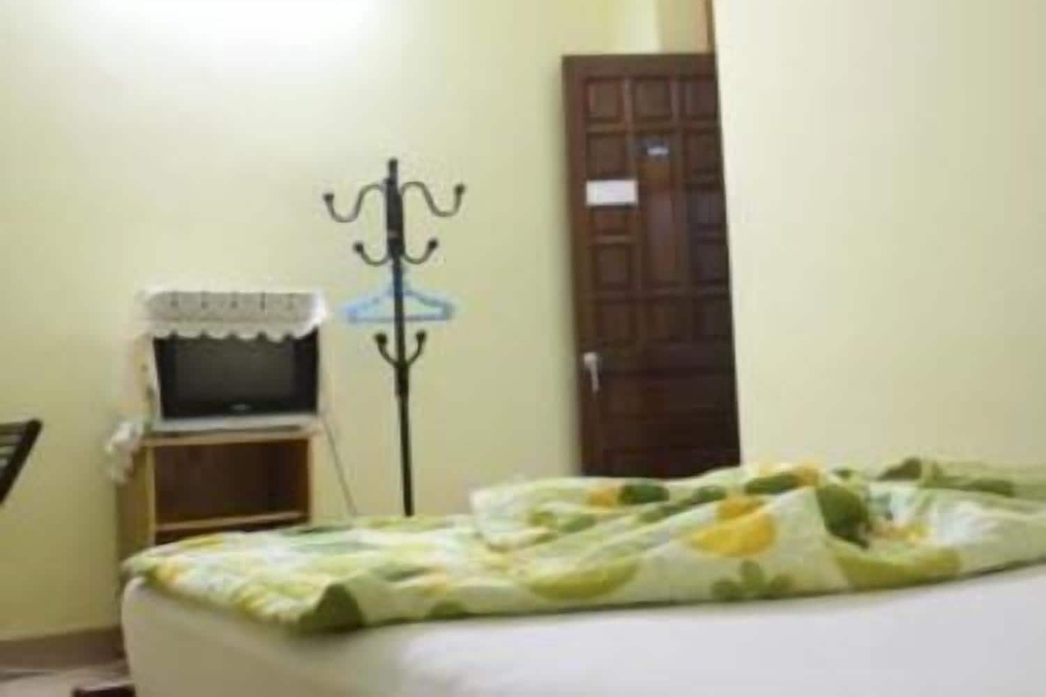 Una habitación con una cama, un televisor sobre un mueble bajo, un perchero y una puerta.