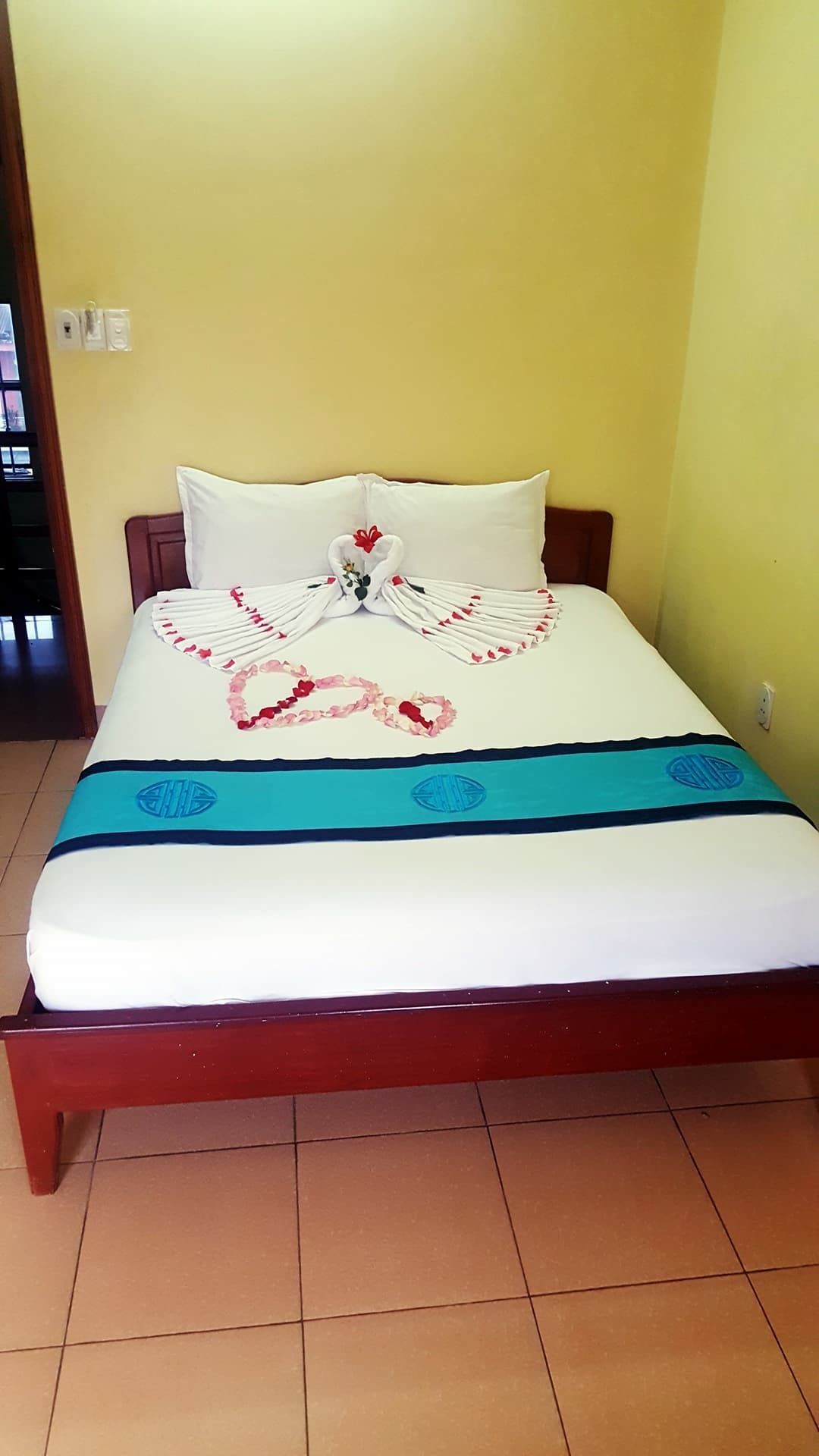 Un lit avec un matelas blanc, une couvre-lit bleue ornée d’une bordure décorative et un arrangement floral posé sur le lit.